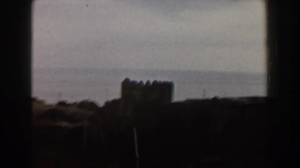 1960 Italy frame with a dark crenellated building silhouette in the foreground and the sea stretching behind it.