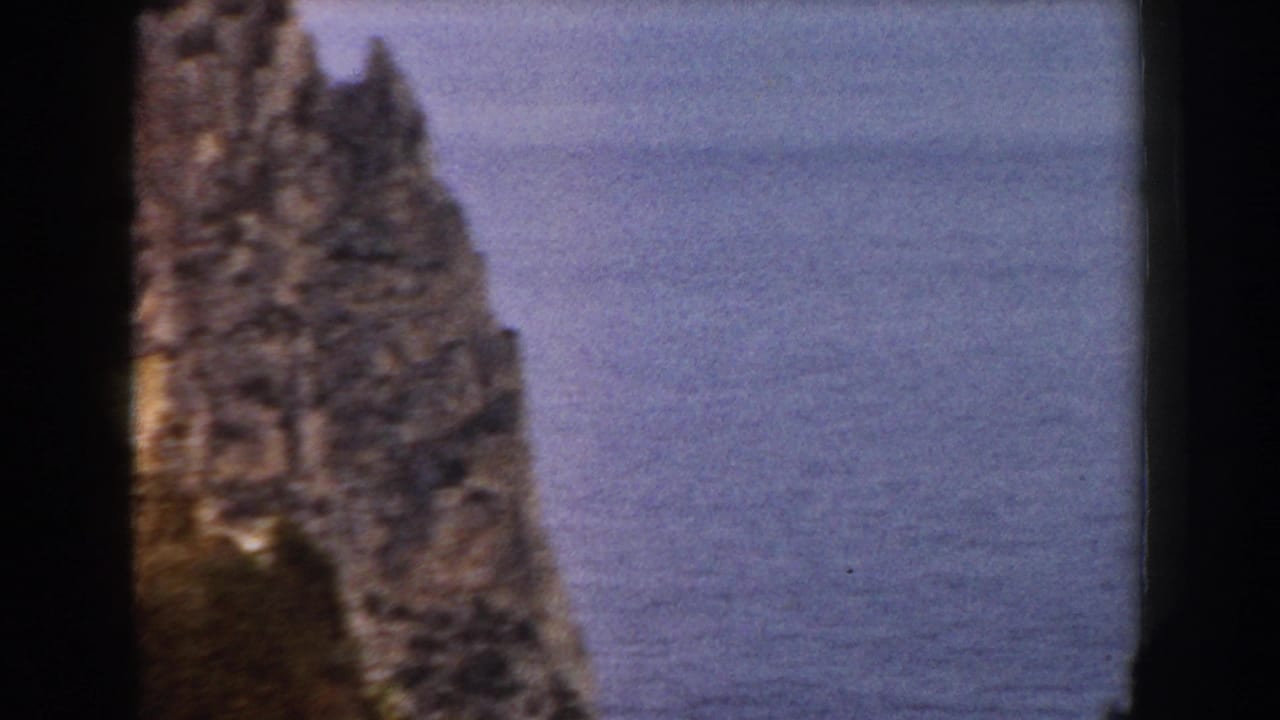Narrow jagged rock stack framed against calm ocean water.