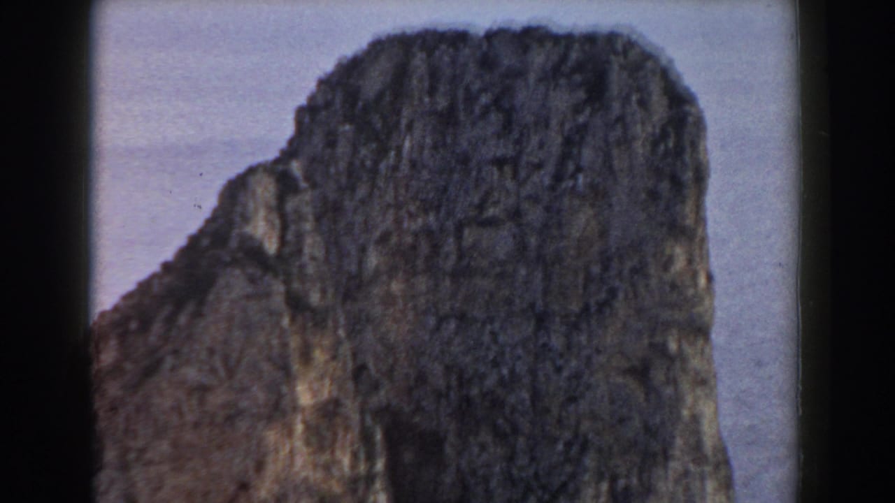 1960 Italy 8mm frame showing a large rocky mountain or cliff face with soft focus and dark film borders.