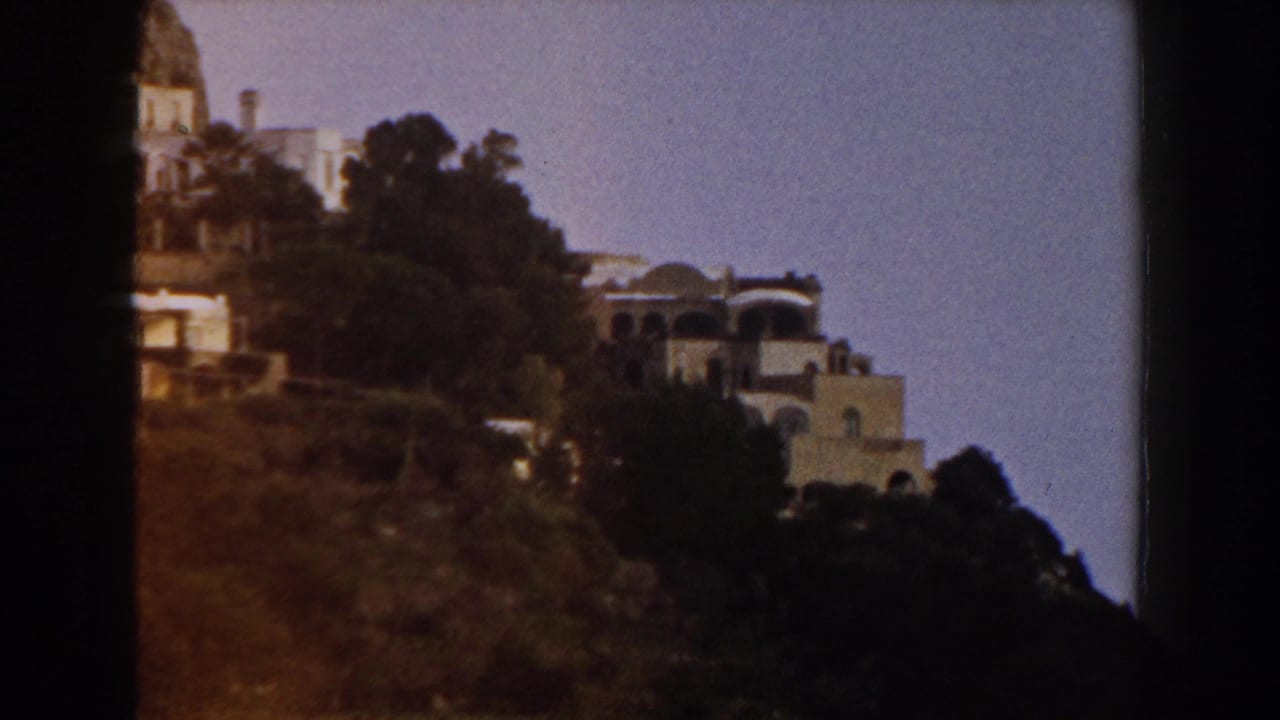 White hillside buildings and trees seen across a sunlit slope.