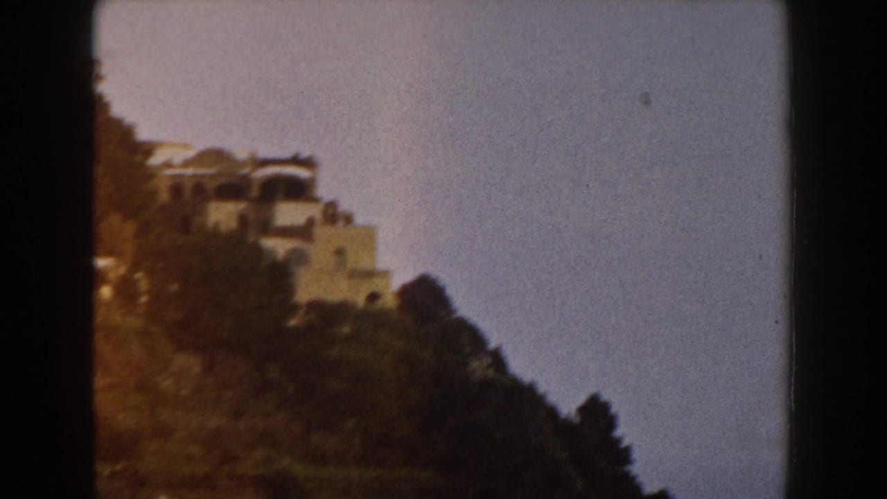 Distant light-colored building on a steep wooded hillside beneath a pale sky.