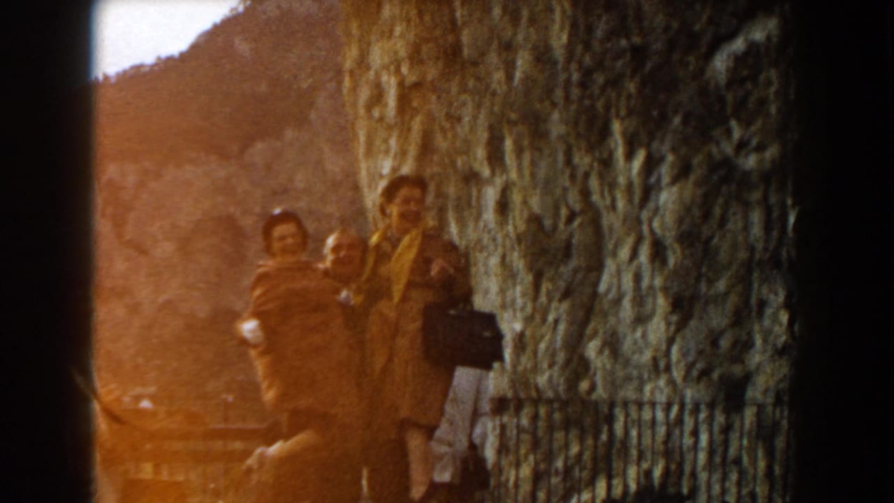 Adults standing near a rugged cliff wall with trees and hillside behind them.