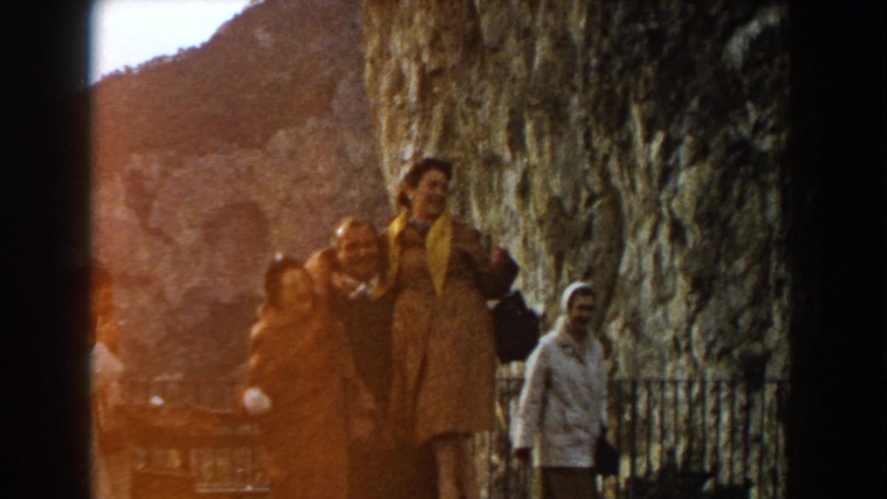 Tourists near a large textured rock wall with another person in a light coat nearby.