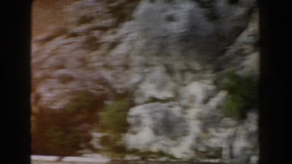 Soft, motion-blurred 8mm frame of an Italian rocky slope with shrubs and warm earth tones along the roadside.