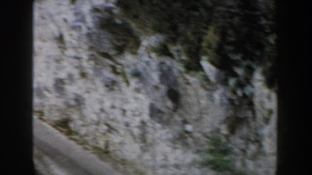 1960 8mm footage from Italy appears to show a paved mountain curve beside a pale rocky cliff with scattered vegetation.
