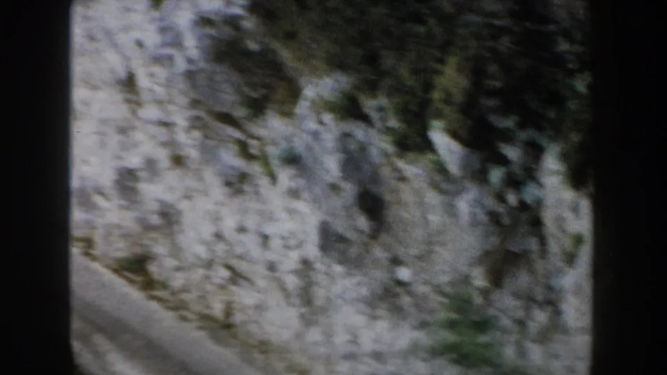 1960 8mm footage from Italy appears to show a paved mountain curve beside a pale rocky cliff with scattered vegetation.