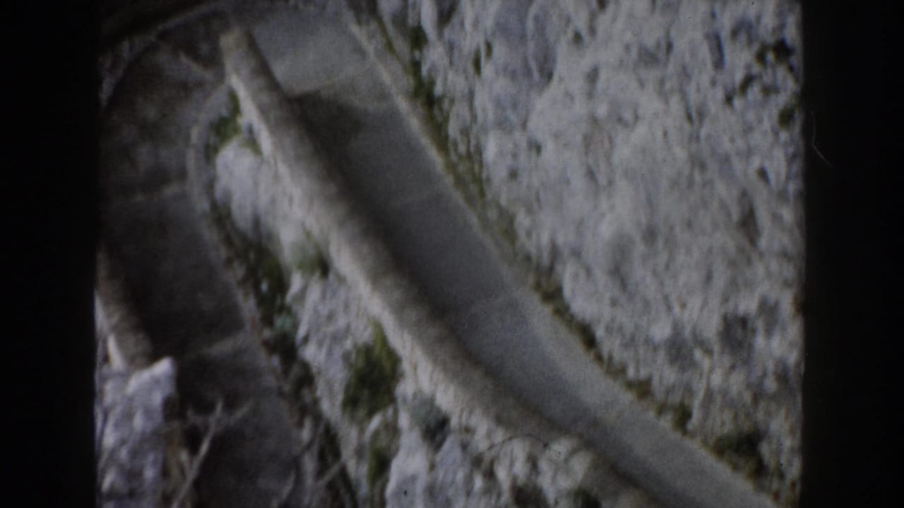 Curving paved edge along a steep rock wall with sparse greenery.