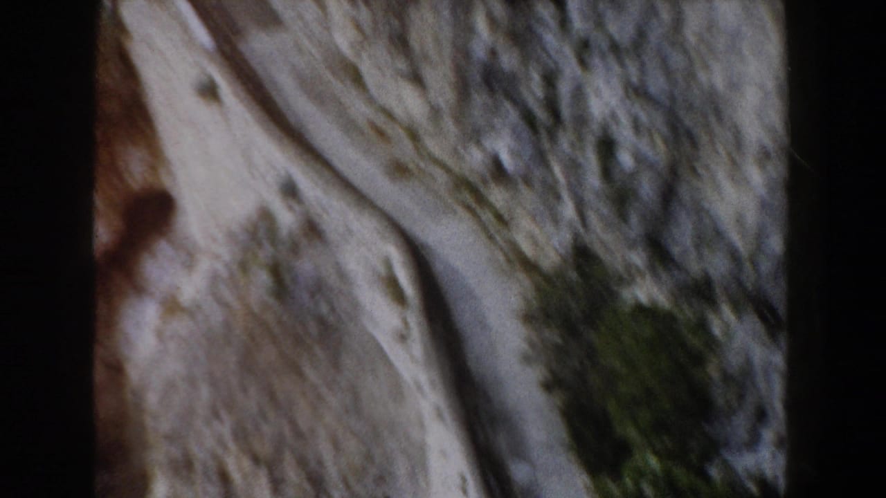 Forward-moving 8mm travel view in Italy showing a road cut into pale canyon rock with brush on the slope.