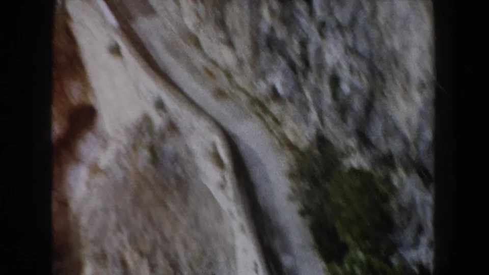 Forward-moving 8mm travel view in Italy showing a road cut into pale canyon rock with brush on the slope.