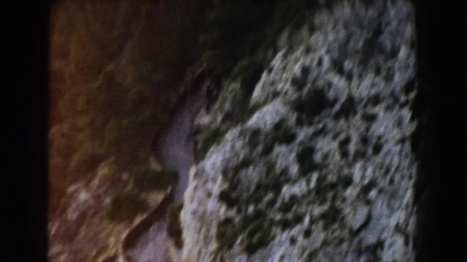 1960 Italy 8mm frame showing a close, soft-focus view of rough cliff rock and shadowed terrain.