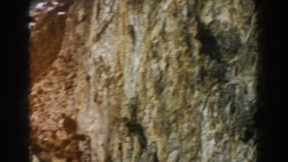 1960 Italy home-movie frame showing a tall rough cliff wall with warm exposure and visible grain.