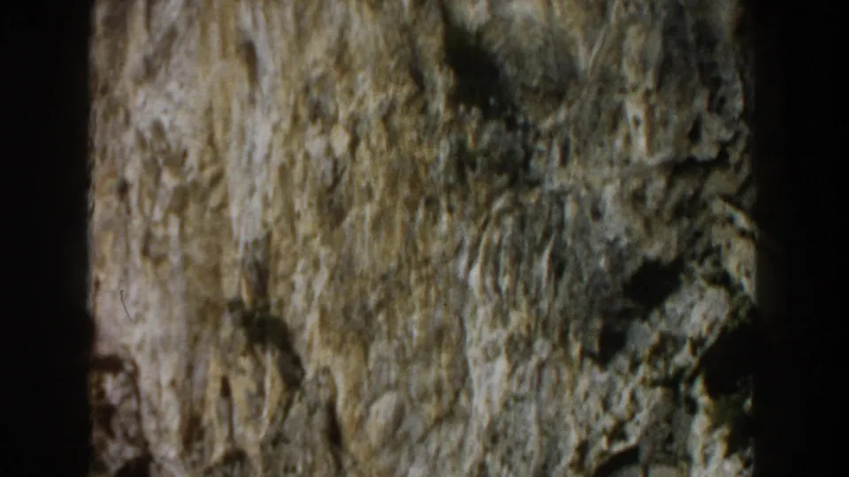 1960 Italy 8mm frame showing a tight view of weathered grey stone with moss or lichen and irregular dark cracks.