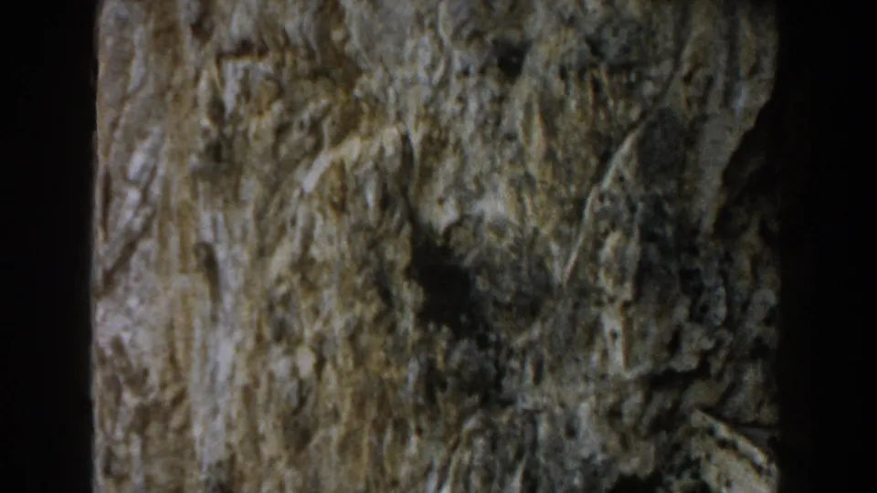 1960 Italy 8mm frame showing rugged grey stone with muted green moss, dark cracks, and visible home-movie grain.