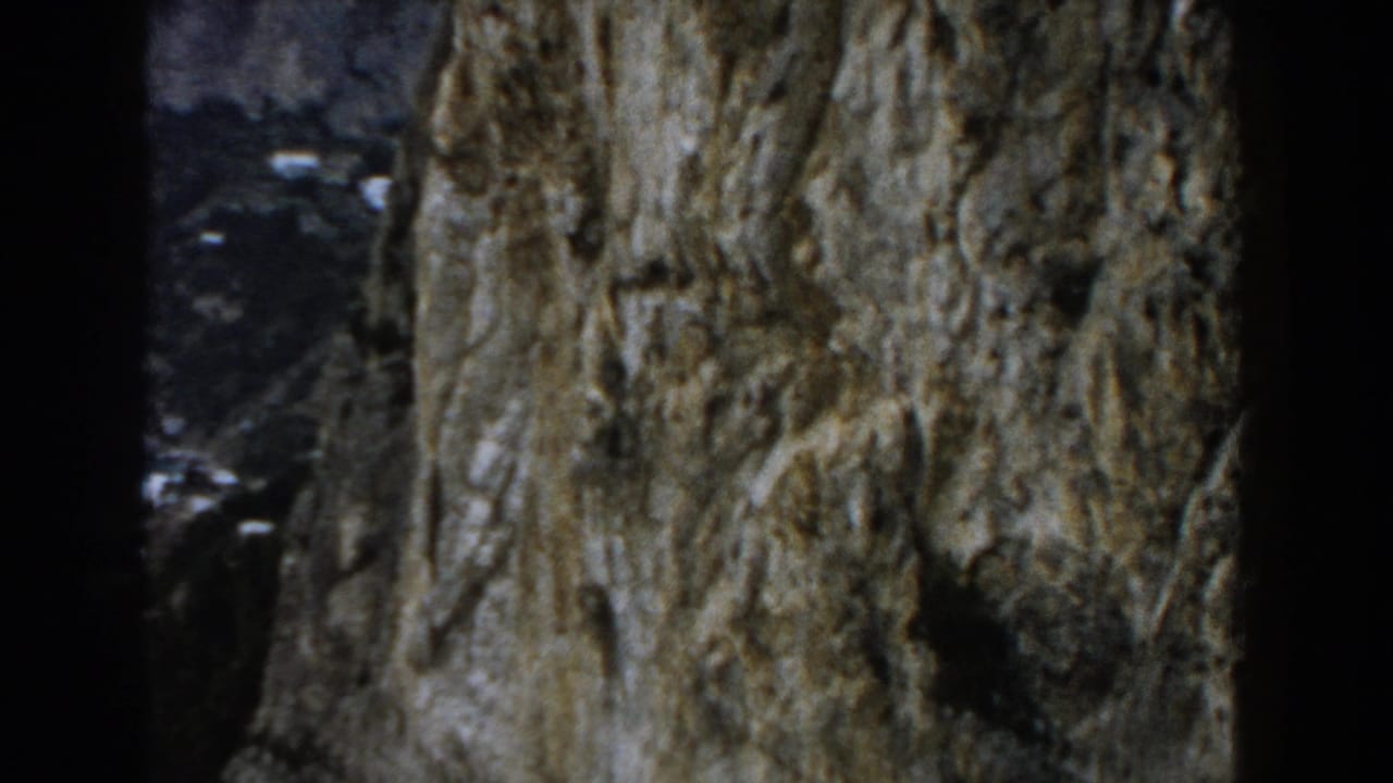 1960 Italy 8mm frame showing a rough cliff face close to camera with distant coastal hillside visible through dark edges.