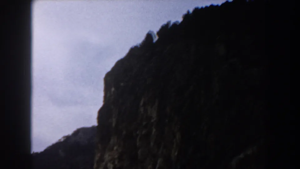 1960 8mm Italy travel frame showing a shadowed rocky cliff edge against a pale blue sky.