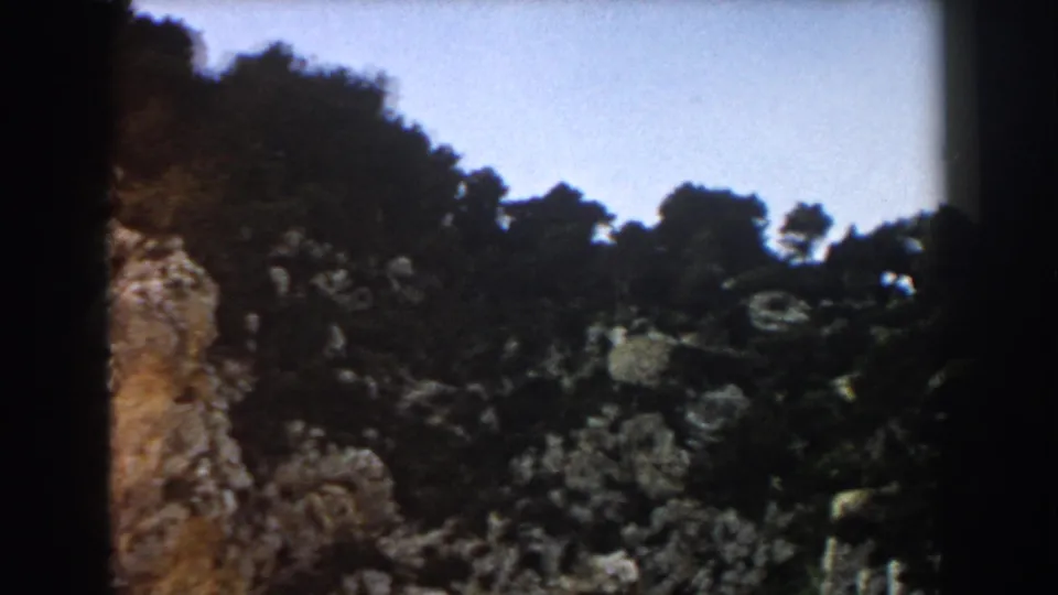 1960 8mm Italy landscape frame showing a steep rocky slope with scattered trees and open sky.