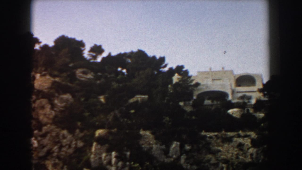 White building partly visible above trees on a rocky cliff.