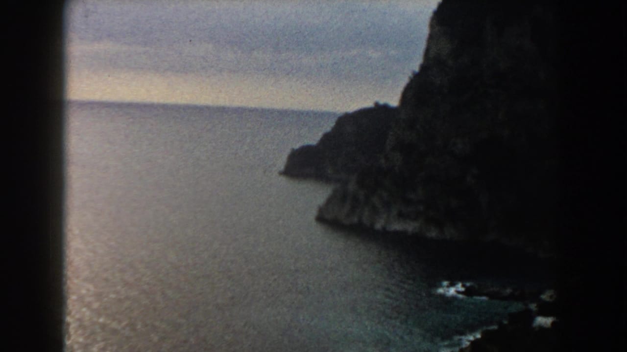 Rocky headland and open water seen through dark film edges.