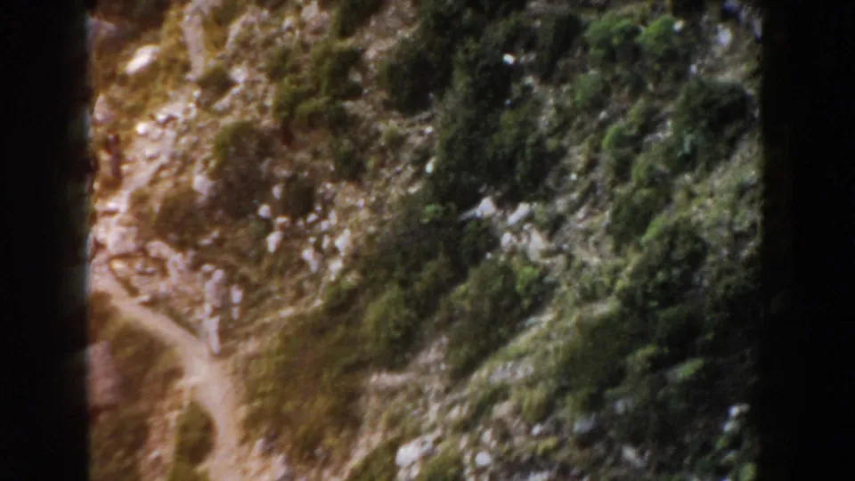 A narrow mountain trail appears among rocks, scrub, and small trees in 1960 Italy home-movie footage.