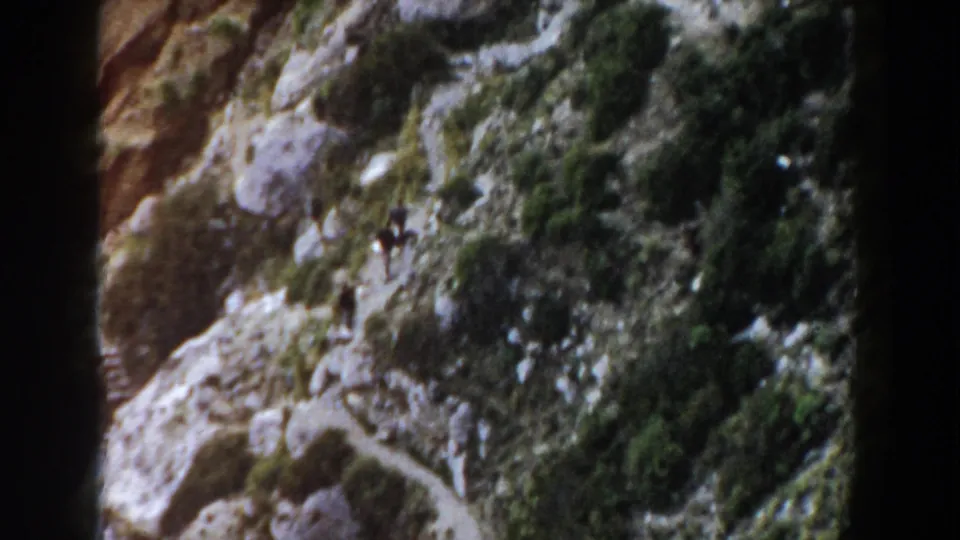 Distant walkers cross a rocky Italian mountainside near a winding dirt trail in 1960 home-movie footage.