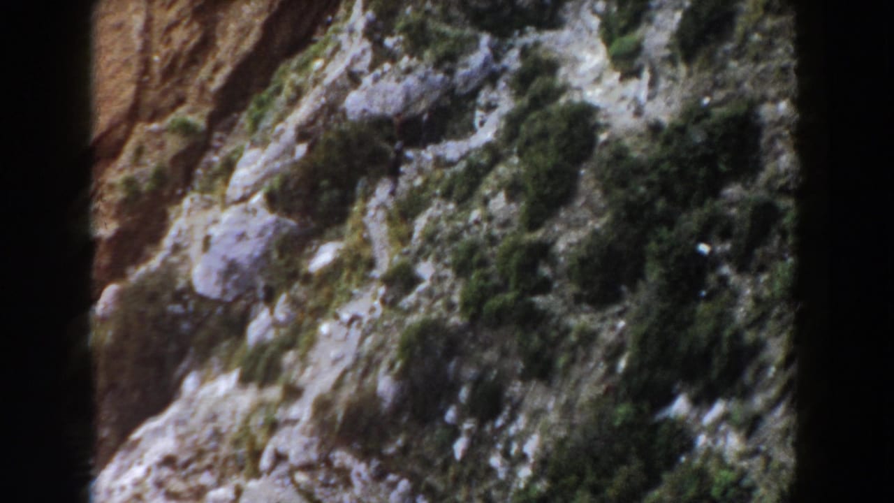 Rocky mountainside with patches of green vegetation and a dark film edge.