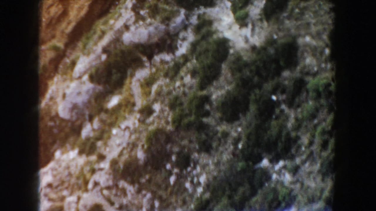 Faded 8mm view of an Italian mountain slope with rocks, brush, and heavy frame-edge shadowing.
