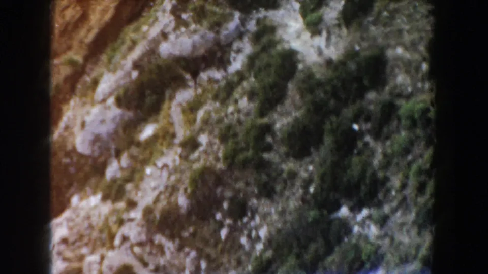 Faded 8mm view of an Italian mountain slope with rocks, brush, and heavy frame-edge shadowing.