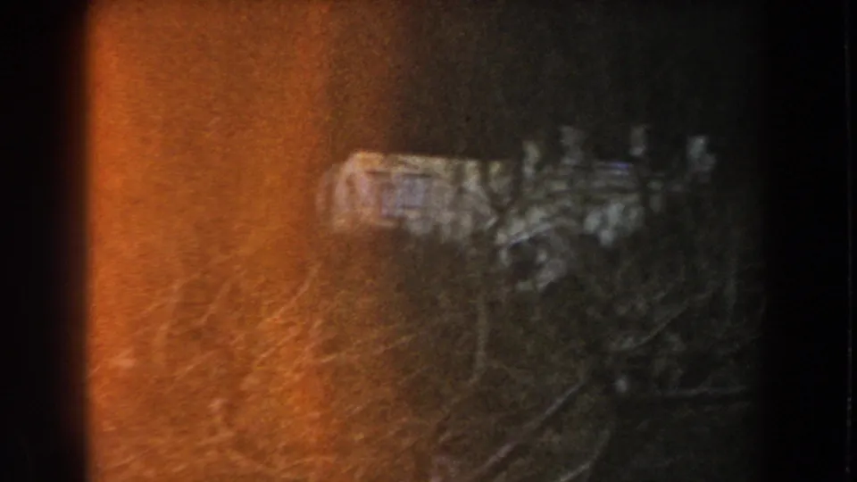 Faded 8mm frame from Italy showing dark woodland, heavy orange flare, and an indistinct pale structure-like object.