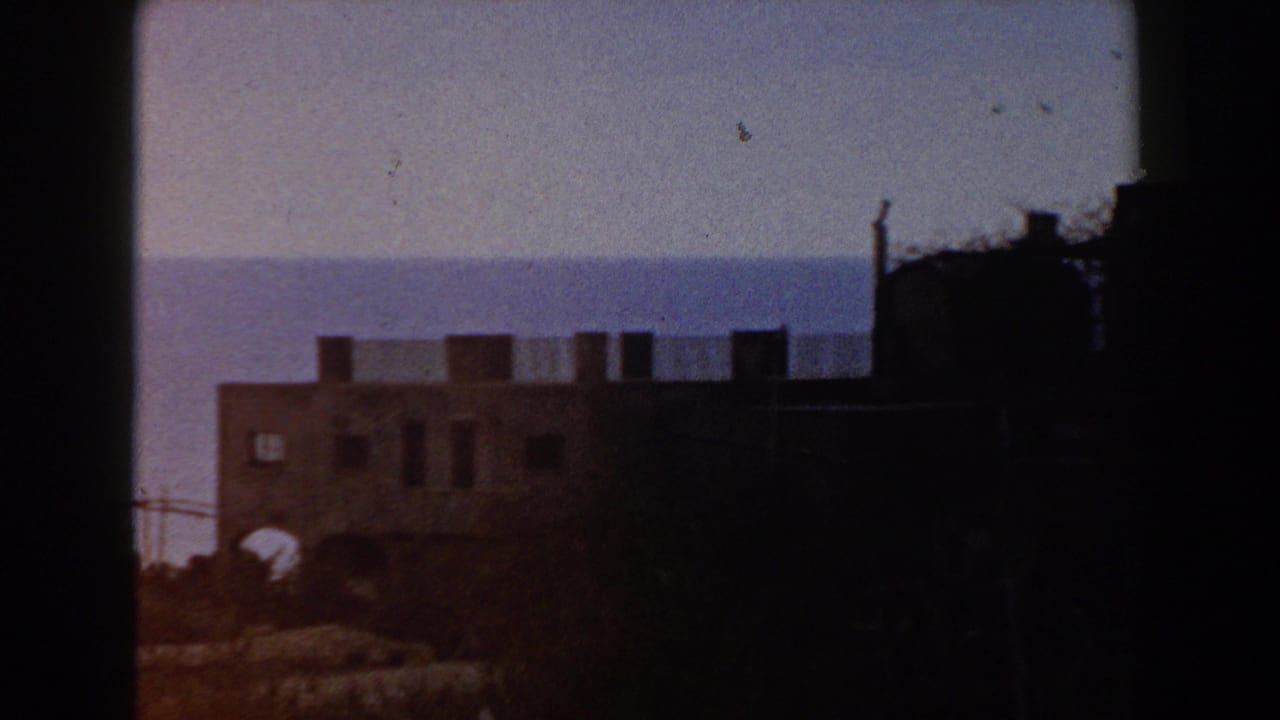 Dark 8mm frame of a stone castle wall with the sea and pale sky behind it.