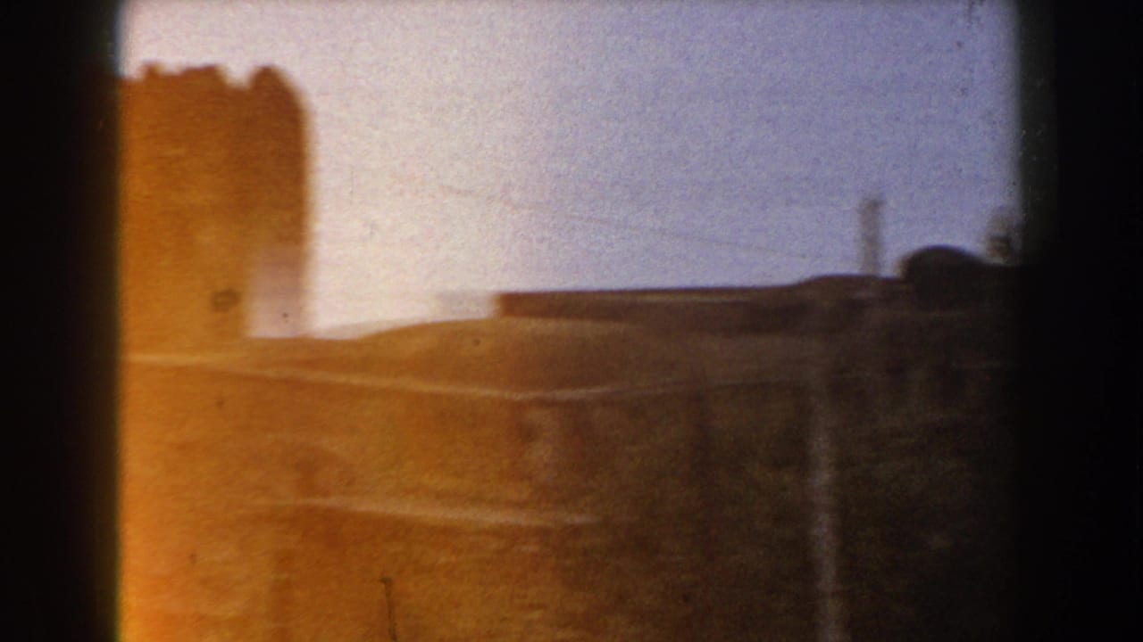 1960 Italy 8mm frame with a warm faded view of crenellated stonework and a low structure near the coastline.