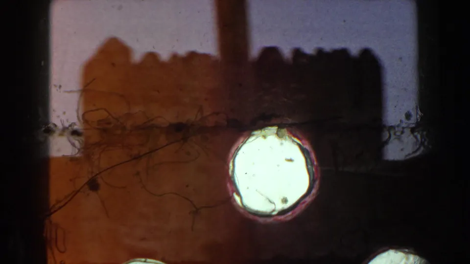 1960 Italy 8mm frame showing castle battlements obscured by scratches, dust, dark edges, and a bright circular light mark.