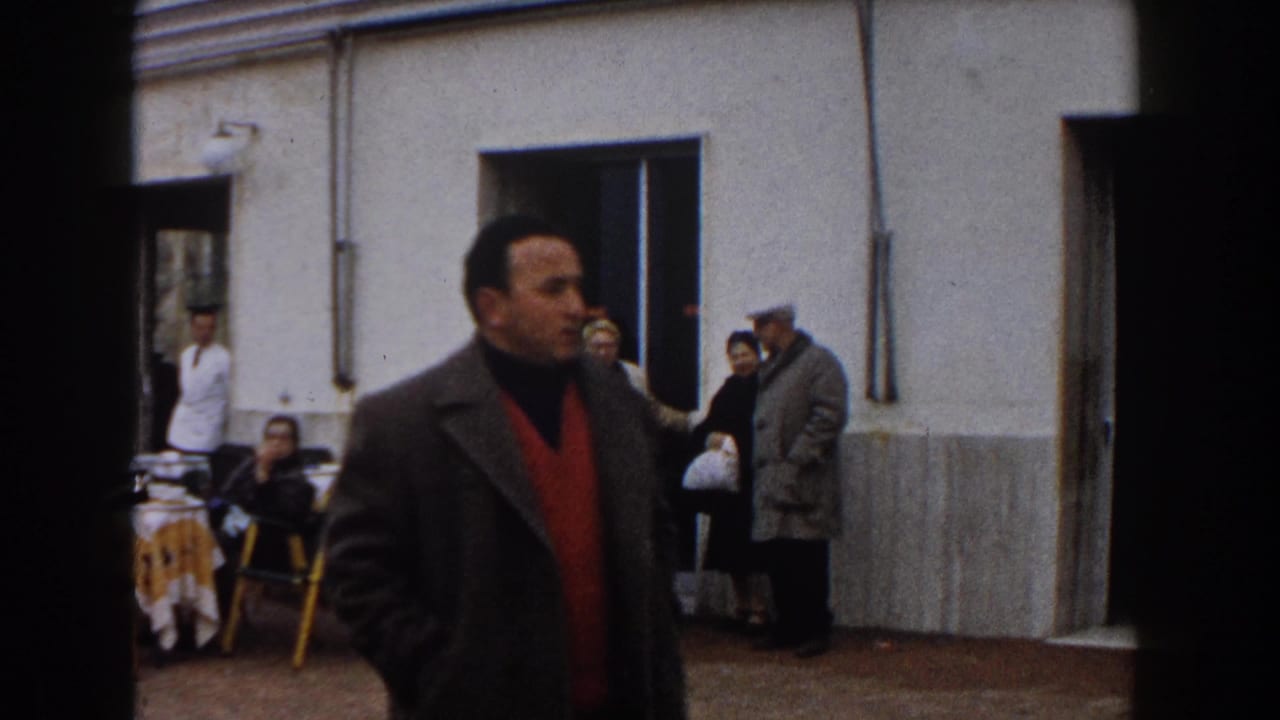 Man in a dark coat and red sweater passes in front of seated people by the doorway.