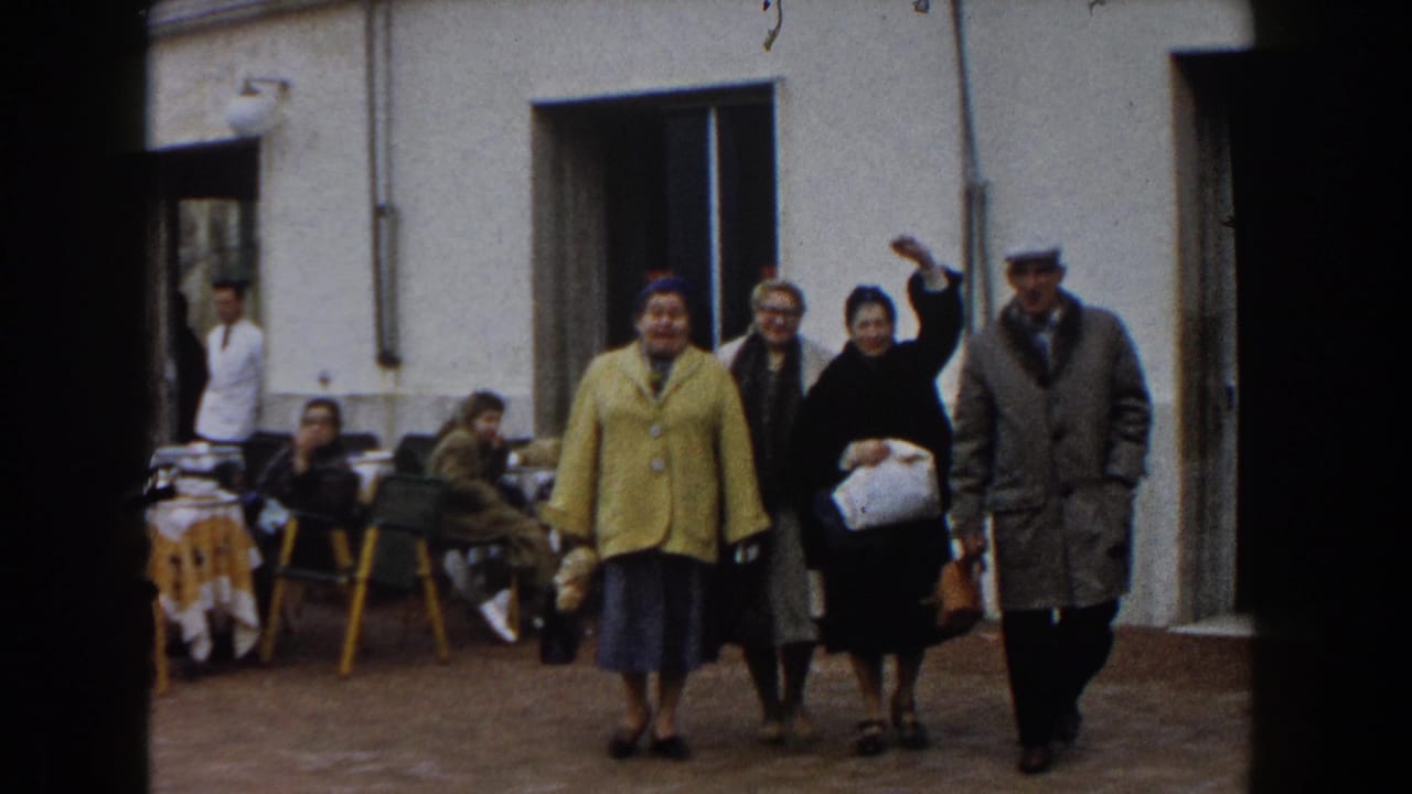 Adults walk toward the camera outside a funicolare station, with cafe tables at left.
