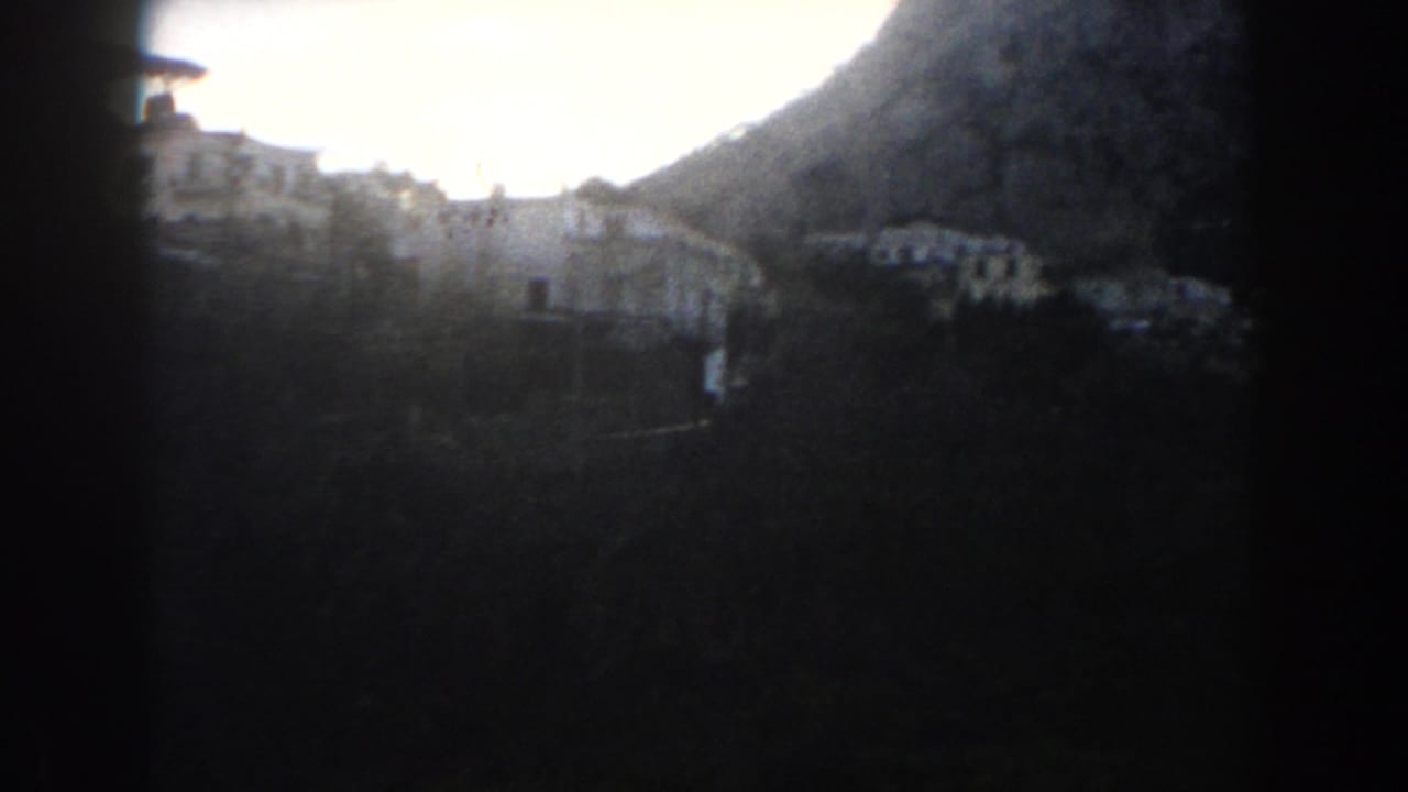 Dark-framed view of white houses on a hillside below a mountain.