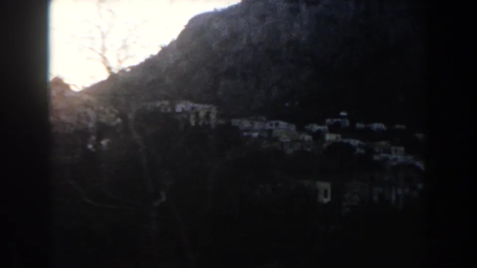 Shadowed 1960 8mm view across an Italian mountain village, with small light-colored buildings scattered along the slope.