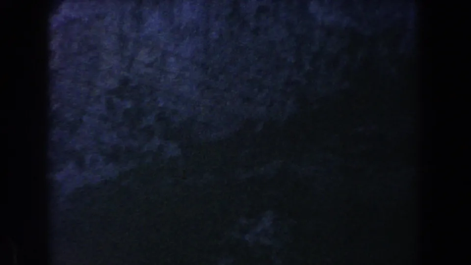 Underexposed 1960 8mm frame from Italy with a dark hillside, faint vegetation, and only limited village detail visible.