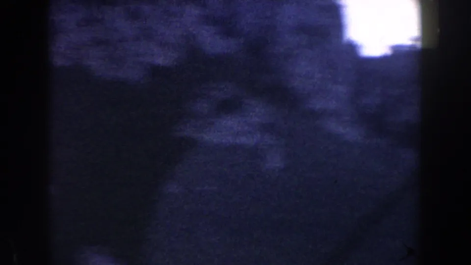 1960 Italy 8mm frame showing a very dark dusk landscape with a pale overexposed patch near the top right.