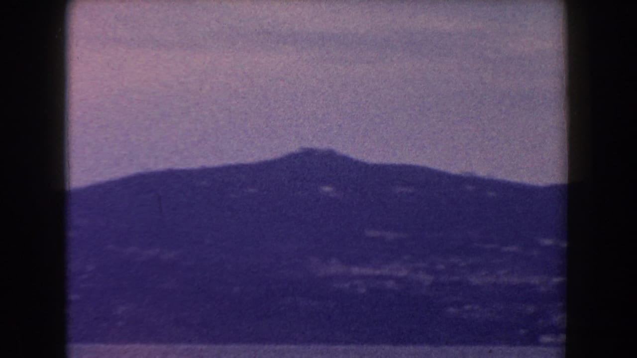 1960 Italy 8mm frame showing a distant mountain ridge in haze beneath a muted sky, with dark gate edges visible.