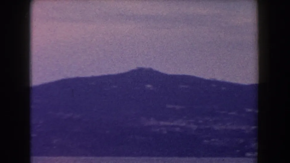 1960 Italy 8mm frame showing a distant mountain ridge in haze beneath a muted sky, with dark gate edges visible.