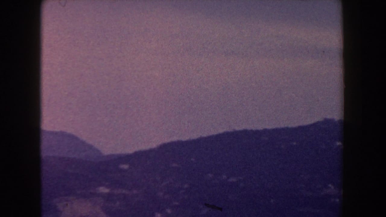 1960 Italy 8mm frame with layered hills and mountain slopes receding into haze, split by a dark film gate edge.