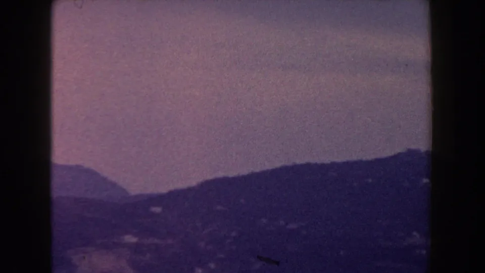 1960 Italy 8mm frame with layered hills and mountain slopes receding into haze, split by a dark film gate edge.
