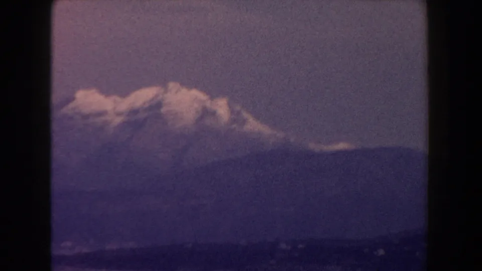 1960 Italy 8mm frame centering a snow-capped mountain summit over a dark ridge with visible grain and gate borders.