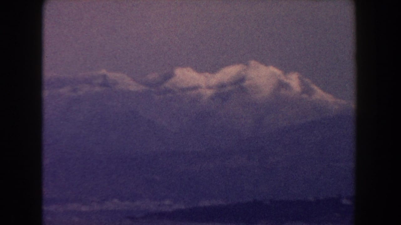Snow-capped mountain ridge above dark water with soft purple film color shift.