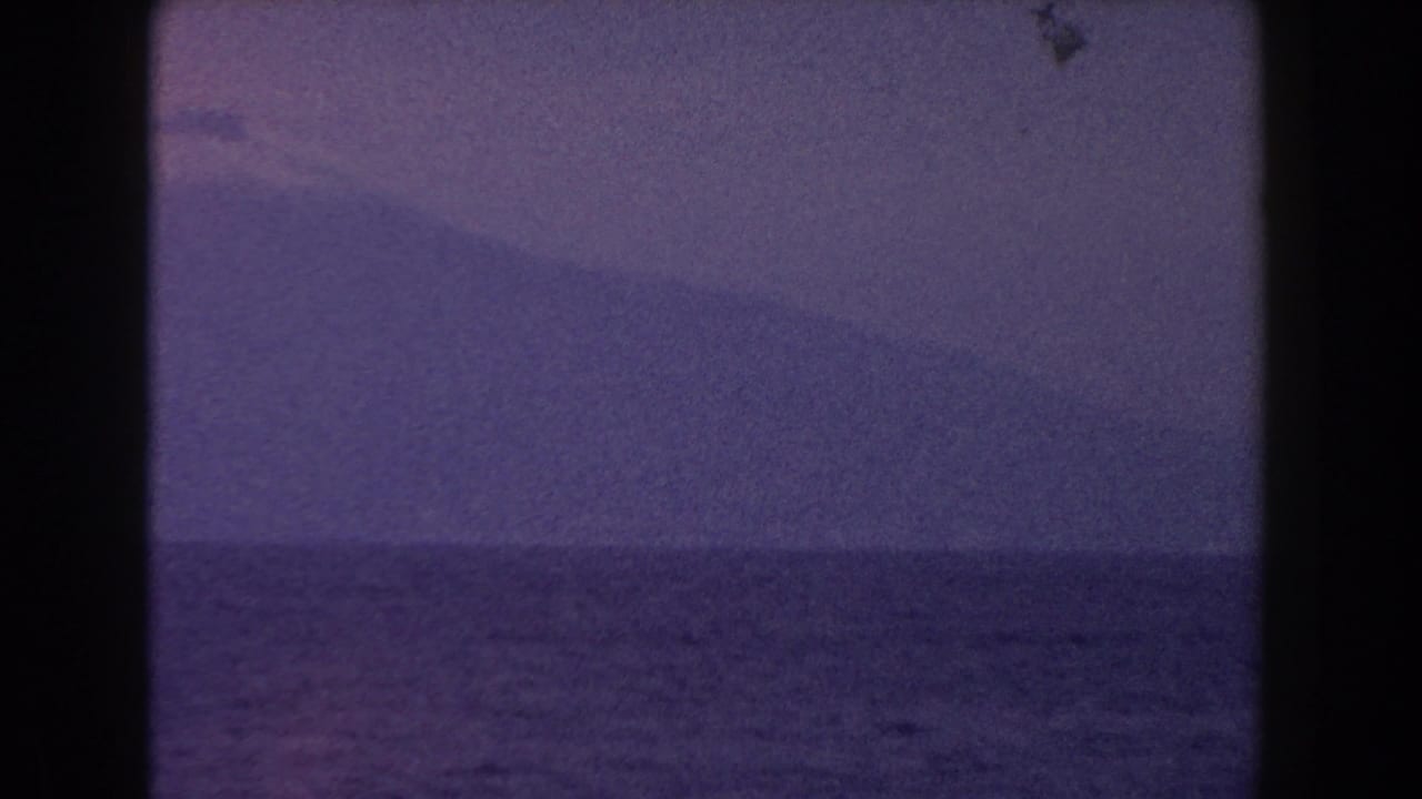 1960 Italy 8mm frame showing open water and a distant snow-capped mountain in soft blue-purple light.