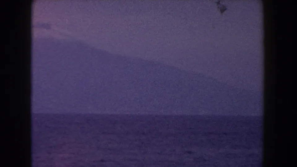 1960 Italy 8mm frame showing open water and a distant snow-capped mountain in soft blue-purple light.