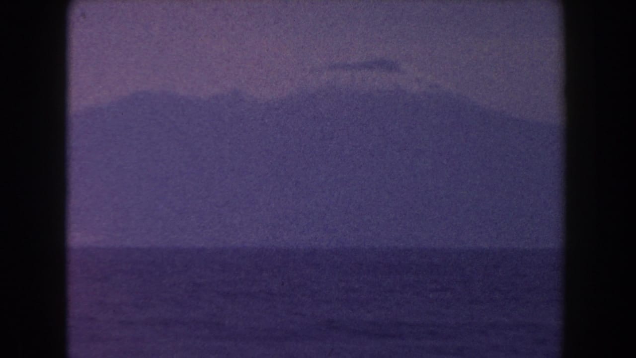 Distant mountain across a calm ocean under a hazy purple sky.