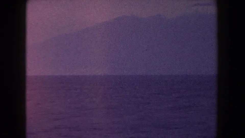 1960 Italian 8mm frame with a dark mountain form across the ocean and pink-purple color fading in the sky.