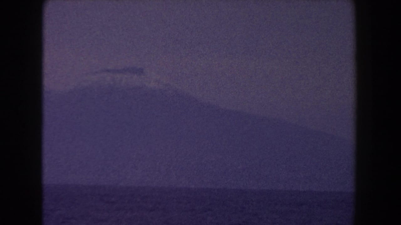 Hazy mountain silhouette across open water with dark film-frame edges.