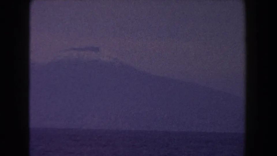 1960 Italian 8mm frame showing a distant mountain silhouette beyond hazy water, seen through dark frame edges.