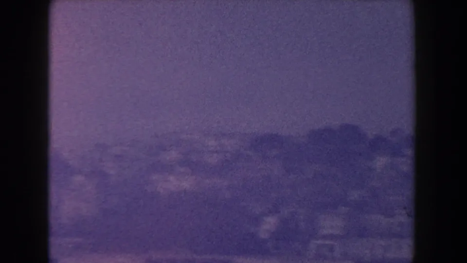 Hazy 1960 Italy shoreline view with distant hills and low buildings, framed by dark window dividers.